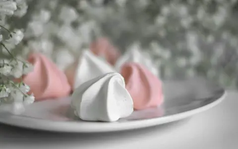 Douceur aérienne de meringue italienne rose et blanche sur une assiette, avec des petites fleurs en arrière-plan.