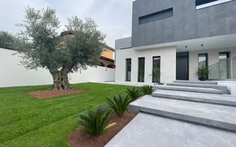 Moderna casa con fachadas color gris y blanco, escaleras de mármol y un olivo centenario en el jardín.