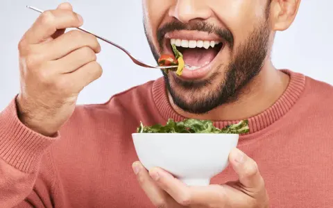 Mann isst Salat, achtet auf die richtige Anzahl, wie oft kauen, für eine gute Verdauung.