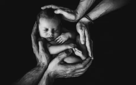 Mani adulte proteggono un neonato addormentato, simbolo di amore e cura. Un futuro di bilinguismo bambini inizia qui.