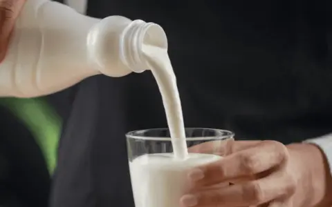 Kefir, naturalny probiotyk, pomaga zwalczać grzybicę jamy ustnej. Biały napój leje się z butelki do szklanki.