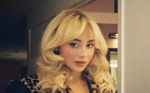 Frau mit voluminösem blondem Haar und Leopardenmuster-Jacke.
