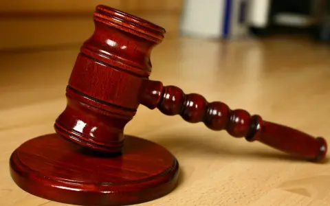 Młotek sędziowski na drewnianym stole. Symbolizuje sprzedaż mieszkania z wpisem komorniczym i decyzje prawne.
