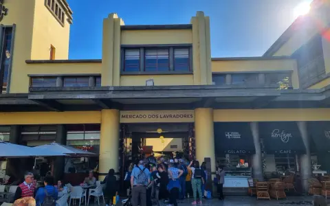 Menschen drängen sich vor dem Mercado dos Lavradores, einem gelben Gebäude mit Cafés und Geschäften.
