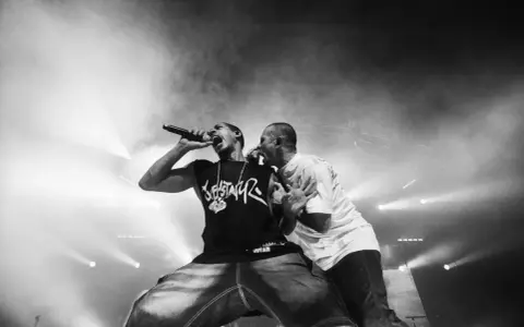 Deux rappeurs en pleine performance, l'un tenant un micro, l'autre le soutenant. Une scène intense qui illustre la puissance du hip hop en France.