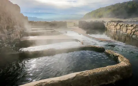 Tierras de vapor y agua en las termas naturales Galicia. Un paisaje sereno con piscinas escalonadas y muros de piedra.
