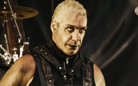 Till Lindemann młody, w skórzanym gorsecie, z mokrymi włosami i intensywnym spojrzeniem, gotowy do występu na scenie.