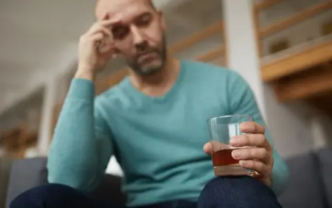 Mężczyzna z bólem głowy trzyma szklankę alkoholu, być może doświadczając reakcji disulfiramowej objawy.