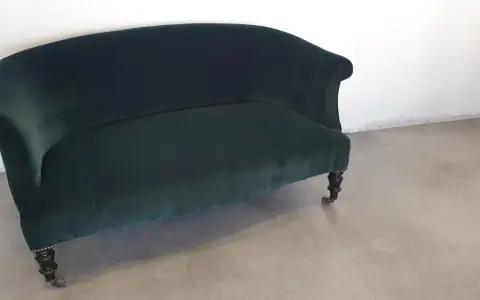 Banquette Napoléon III en velours vert profond, aux pieds sculptés et roulettes. Un meuble élégant pour un salon d'époque.