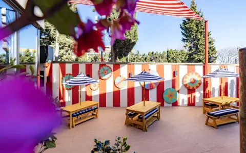 Terraza de restaurantes con zona infantil en Madrid, decorada con rayas rojas y blancas y coloridos adornos circulares. Mesas de madera con sombrillas a rayas invitan a disfrutar.