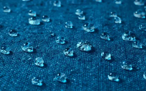Gouttes d'eau perlant sur un tissu bleu, illustrant comment imperméabiliser un tissu naturellement.