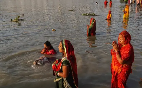 Mujeres rezan en el río Ganges, con vestimentas coloridas y el agua hasta la cintura.