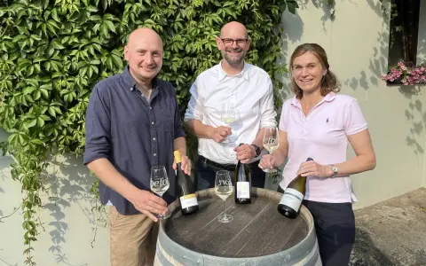 Drei Personen präsentieren Wein. Die Flasche mit Auxerrois Aussprache ist im Fokus.