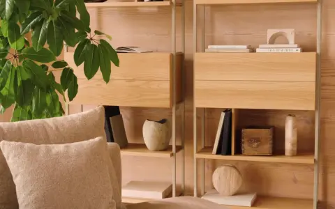 Mysig soffa med kuddar framför en hylla i ljust trä. Perfekt för dansk inredning inspiration med böcker och dekorativa föremål.