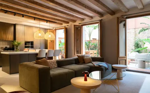 Sofá modular verde con acabado fratasado, mesas auxiliares, lámpara roja y acceso a patio con muebles de exterior.
