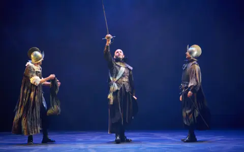 Tres hombres con armadura y espadas en un escenario. El del centro levanta su espada. Escena de "El alcalde de Zalamea".