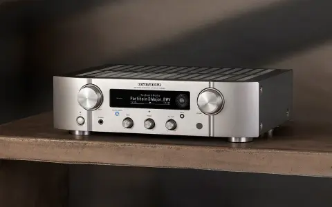 Srebrny wzmacniacz Marantz PM7000N, gotowy do testu, z wyświetlaczem pokazującym utwór muzyczny.