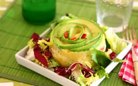 Causa limeña con aguacate en espiral y ensalada fresca, servida en plato blanco.