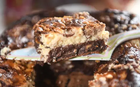 Ein Stück saftiger "friss dich dumm kuchen vom blech" mit Schichten aus Schokolade, Käsekuchen und Nüssen wird serviert.