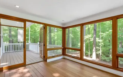 Amplio solárium con grandes ventanales y puertas de madera que dan a un porche. El color ventanas pvc de madera complementa el entorno boscoso.