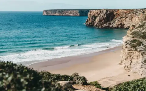 Ein einsamer Surfer genießt die Wellen am Sagres Strand, umgeben von steilen Klippen und dem weiten Atlantik.