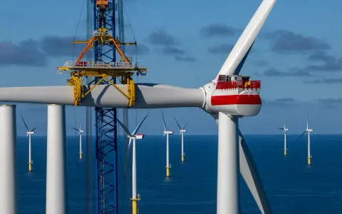 Bau eines Offshore-Windparks für die **Energie Niederlande**. Ein Kran hebt ein Rotorblatt einer riesigen Windkraftanlage im Meer.