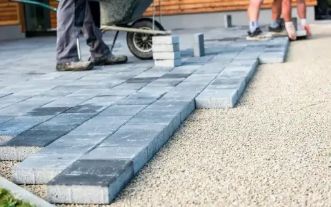 Układanie betonowych płyt na żwirze. Pracownicy tworzą ścieżkę, gdzie beton zamiast kostki staje się nowoczesnym rozwiązaniem.
