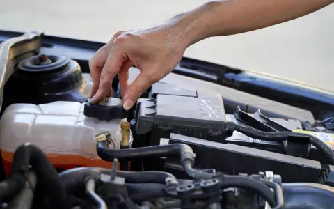 A hand twists the cap on a car's coolant reservoir, a step in learning how to dispose of antifreeze safely.