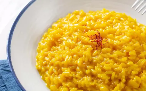 Un cremoso risotto alla milanese, giallo intenso grazie allo zafferano, guarnito con fili rossi.