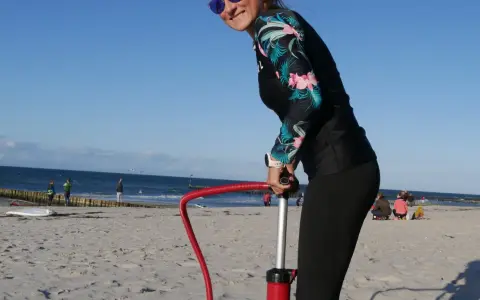 Frau pumpt SUP auf. Am Strand bereitet sie sich auf Wassersport vor.