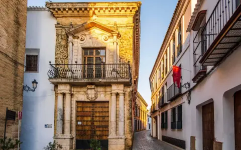 Calle empedrada flanqueada por edificios históricos, un ejemplo de los pueblos bonitos de Sevilla. Fachada de piedra dorada con balcón y puerta de madera.