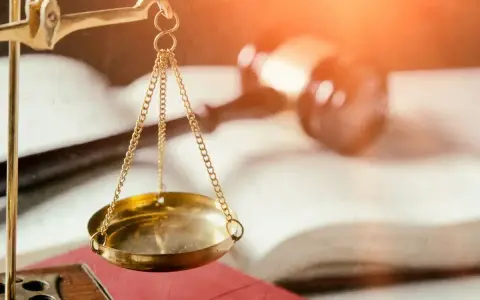 Złota waga sprawiedliwości na tle otwartej księgi i młotka sędziowskiego.