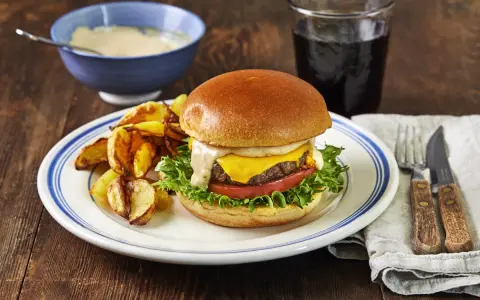 En saftig hamburgare med ost, sallad och tomat, serverad med klyftpotatis och en skål med hemlagad hamburgerdressing.