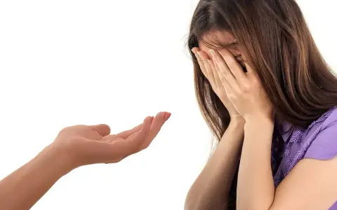 Kobieta płacze, zakrywając twarz dłońmi. Wyciągnięta dłoń oferuje wsparcie, symbolizując trudny moment, jak przyznać się do kłamstwa.