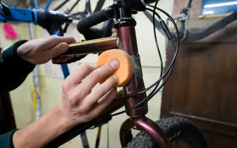 Hände polieren den Fahrradrahmen mit einem orangen Schwamm, um den Fahrradlack auszubessern.