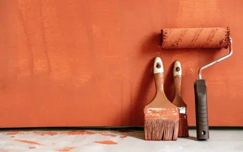 Deux pinceaux et un rouleau à peinture, prêts à rattraper trace de rouleau peinture sur un mur orange texturé.