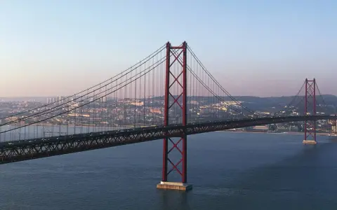Der rote Hängebrücken-Gigant, oft als "Golden Gate Lissabon" bezeichnet, überspannt das ruhige Wasser mit der Stadt im Hintergrund.