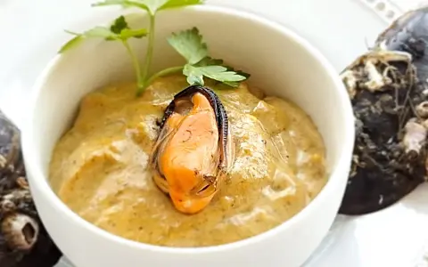 Paté de mejillones cremoso en cuenco blanco, decorado con perejil y mejillones enteros al lado.
