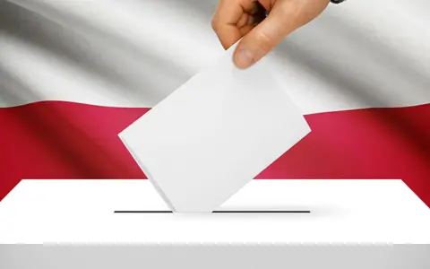 Dłoń wrzuca kartę do urny wyborczej na tle flagi Polski. To symbol ważnych wyborów do parlamentu.