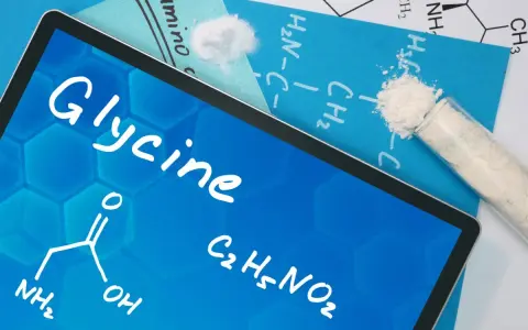 Tablet z napisem "Glycine", wzorem chemicznym i próbówką z proszkiem. Informacje o glicynie i jej dawkowanie.