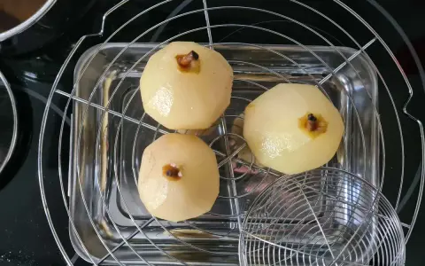Trois poires pochées, prêtes pour une délicieuse recette tarte bourdaloue, égouttent sur une grille.