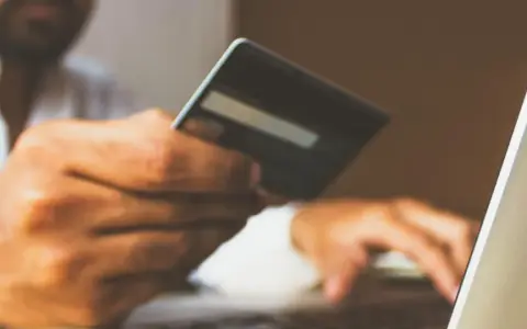 Mężczyzna z kartą płatniczą przy laptopie, zapewniający sobie bezpieczne zakupy w internecie.