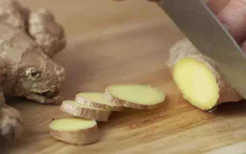 Un pezzo di zenzero fresco viene affettato su un tagliere di legno, mostrando come si mangia questo ingrediente versatile.