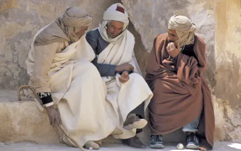 Drei Männer in traditioneller Kleidung sitzen und unterhalten sich. Sie diskutieren vielleicht, was haben Araber erfunden, während sie die Sonne genießen.