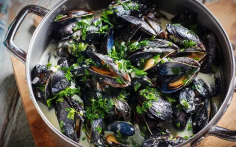En stor gryta med ångande moules marinières, toppad med färsk persilja och serverad i en krämig vitvinssås.
