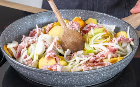 Zutaten für einen herzhaften Hamburger Pannfisch werden in einer Pfanne vermischt: Kartoffeln, Speck und Zwiebeln.