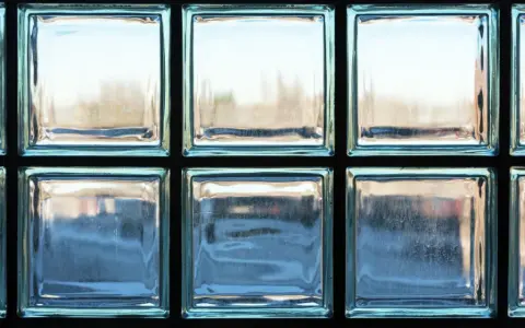Un mur en brique de verre, reflétant la lumière extérieure, crée une ambiance douce et diffuse.
