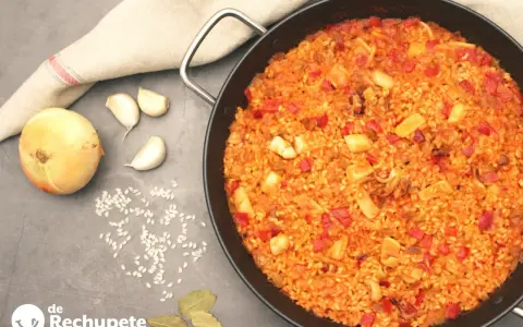 Arroz con calamares en paellera, con ingredientes como cebolla, ajo y pimientos. Un plato delicioso y lleno de sabor.