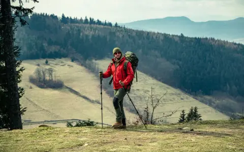 Mężczyzna w czerwonej kurtce i z plecakiem, gotowy do nordic walking. Jak zacząć? Wskazówki dla początkujących.