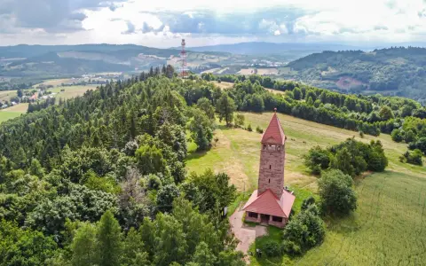 Kamienna wieża widokowa na wzgórzu, otoczona lasami i polami. Jedna z wielu wież widokowych na Dolnym Śląsku, oferująca malownicze krajobrazy.